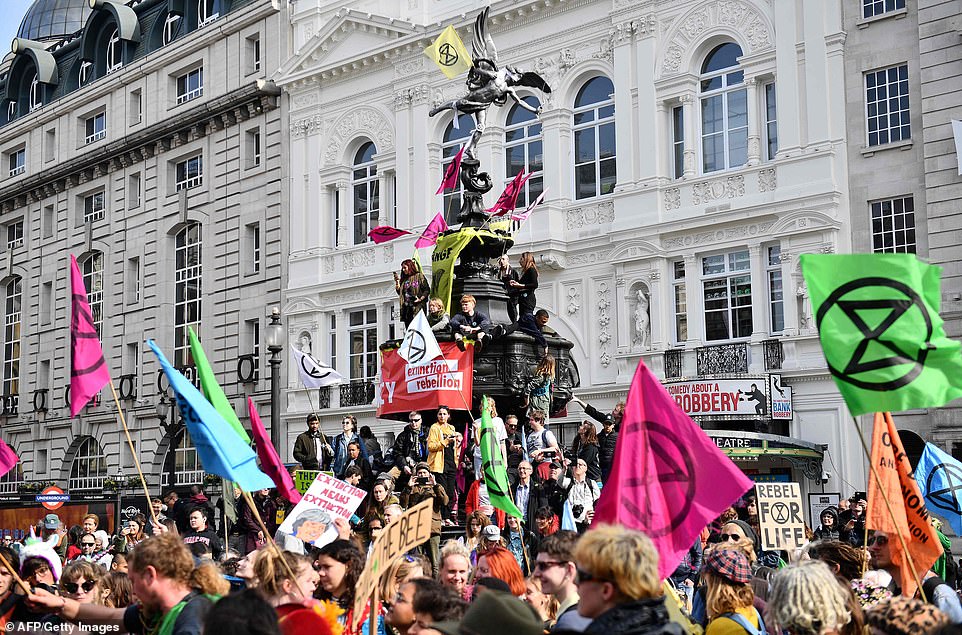 Extinction Rebellion eco-protesters wave flags from the Shaftesbury Memorial Fountain at Piccadilly Circus in London